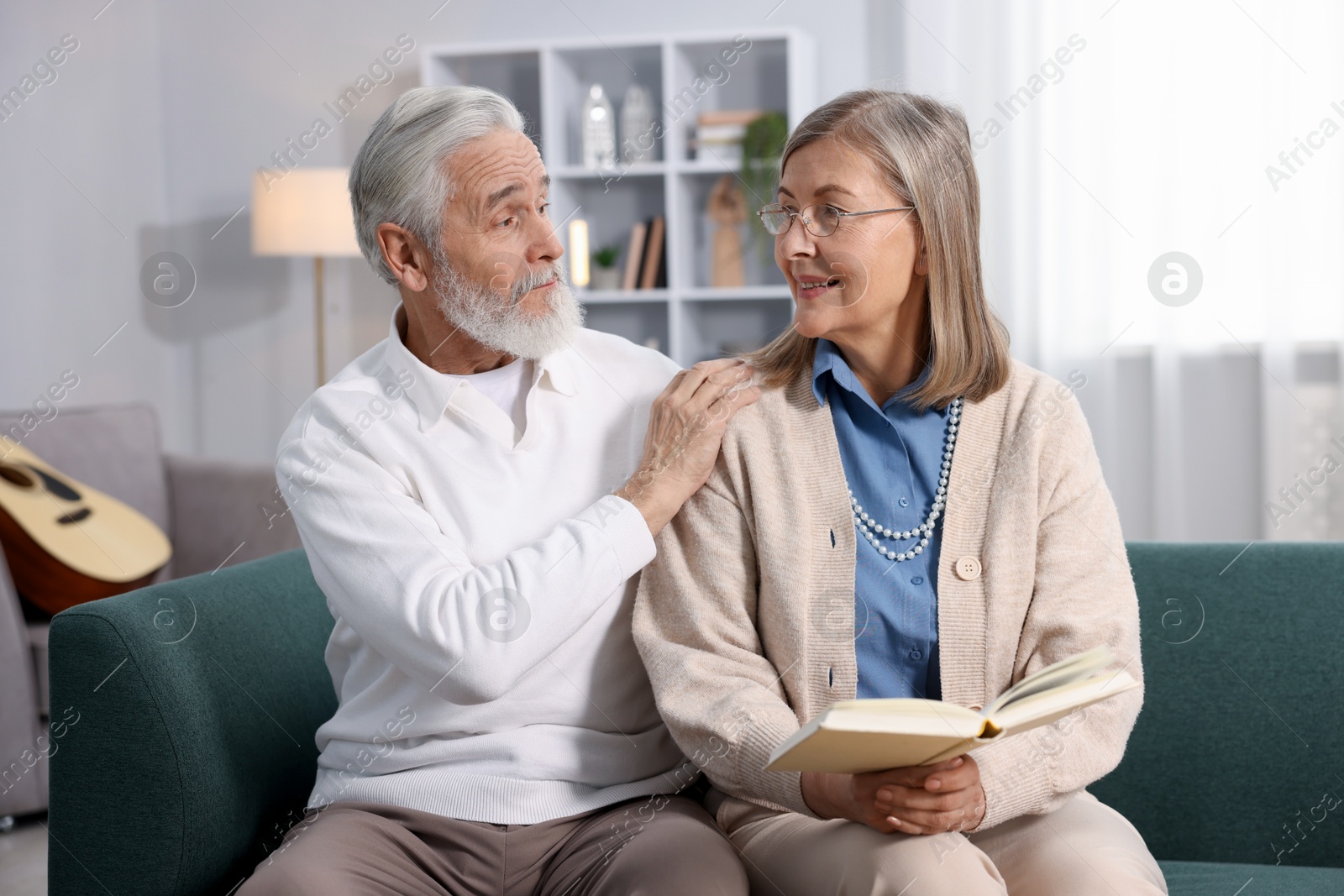 Photo of Happy elderly couple looking at each other on sofa at home