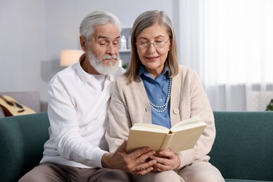 Photo of Cute elderly couple reading book together on sofa at home