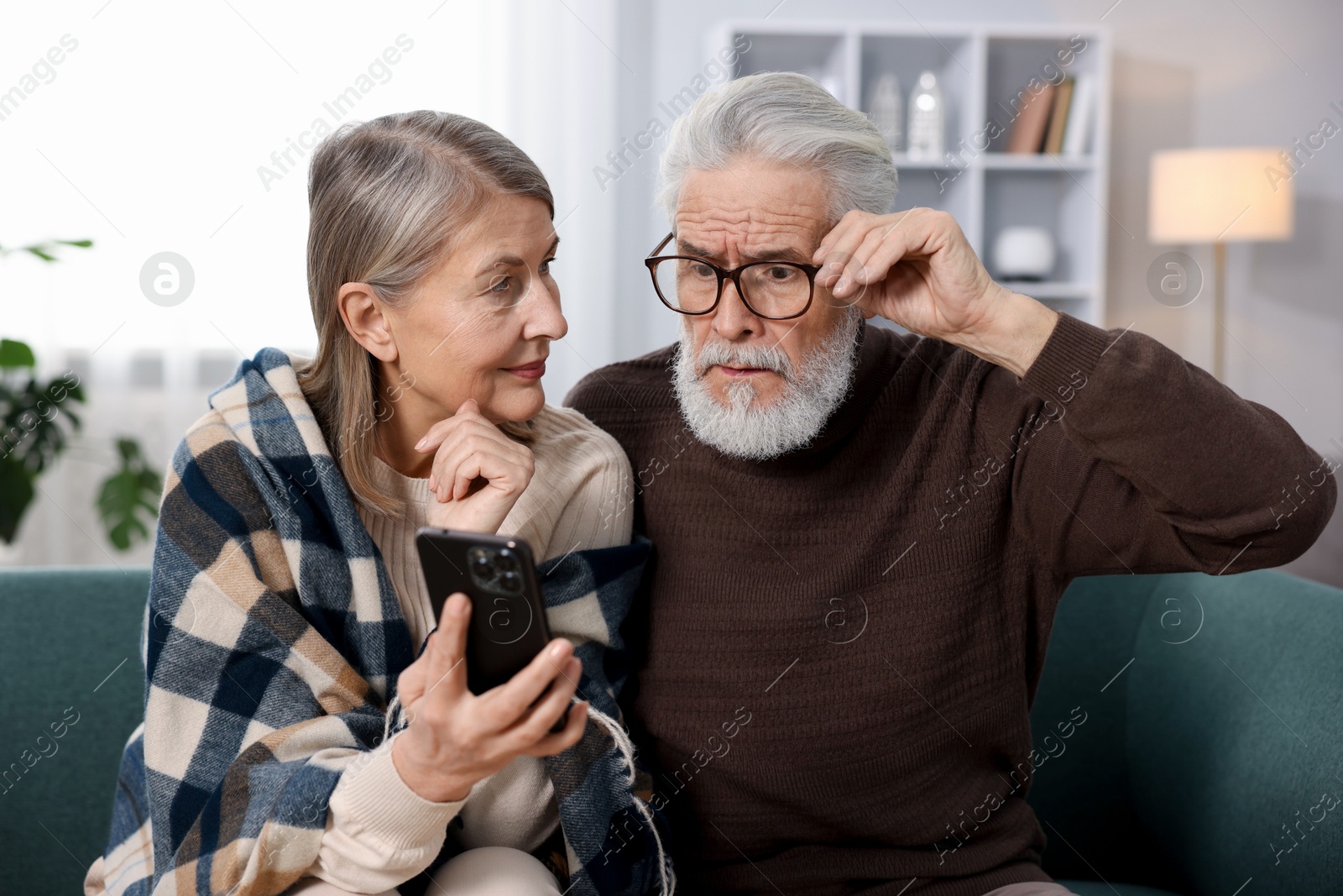 Photo of Cute elderly couple looking at smartphone on sofa at home