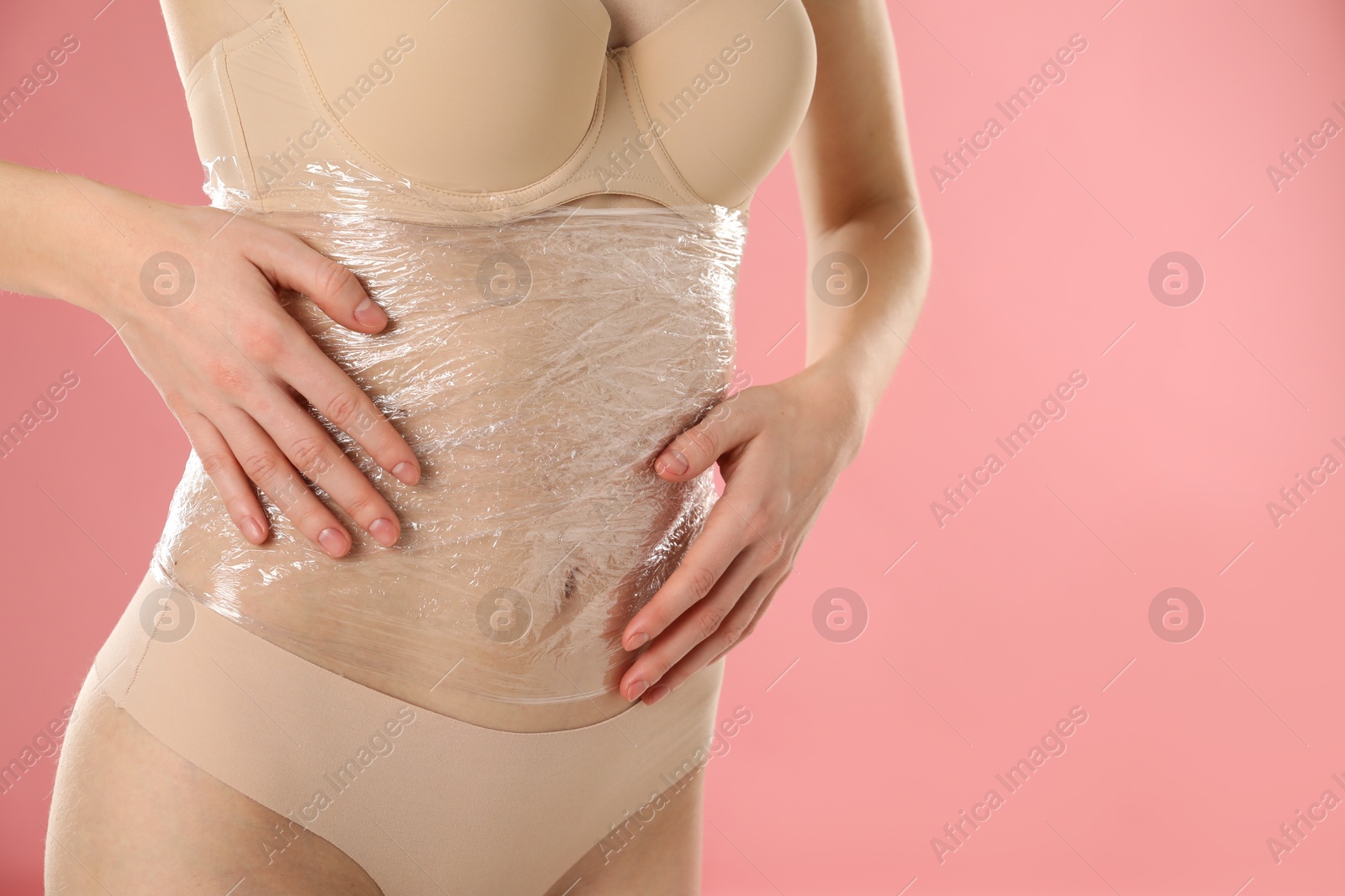 Photo of Woman doing spa body wraps on her belly against pink background, closeup