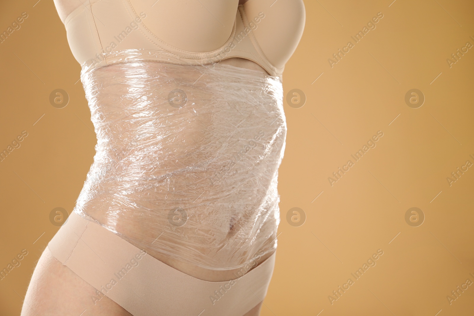 Photo of Woman doing spa body wraps on her belly against beige background, closeup. Space for text