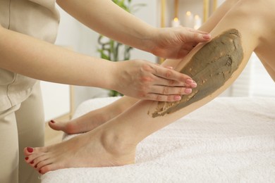 Photo of Esthetician applying cosmetic product for body wraps treatment onto woman's leg in spa salon, closeup