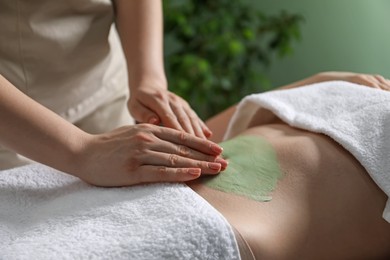 Photo of Esthetician applying cosmetic product for body wraps treatment onto woman's belly in spa salon, closeup