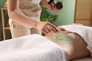 Woman undergoing body wraps treatment in spa salon, closeup