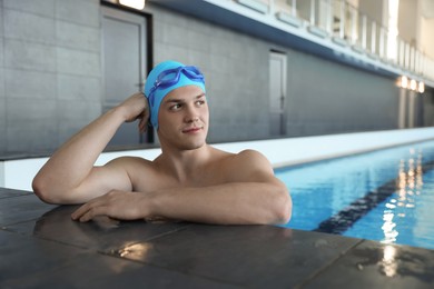 Photo of Young man wearing cap and goggles in swimming pool indoors