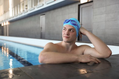 Photo of Young man wearing cap and goggles in swimming pool indoors