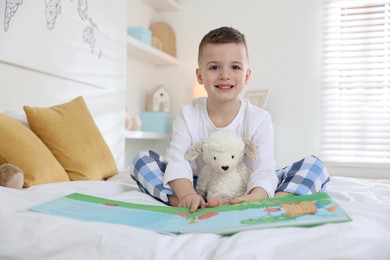 Bedtime. Cute boy with toy sheep reading book on bed indoors