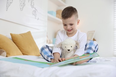 Bedtime. Cute boy with toy sheep reading book on bed indoors