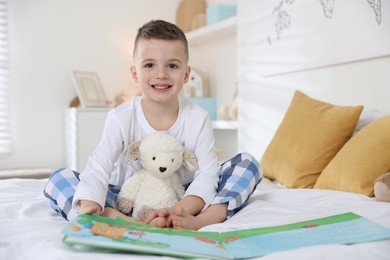 Photo of Bedtime. Cute boy with toy sheep reading book on bed indoors