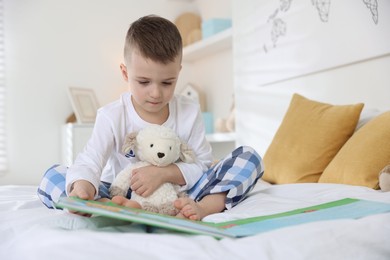 Photo of Bedtime. Cute boy with toy sheep reading book on bed indoors