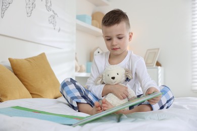 Bedtime. Cute boy with toy sheep reading book on bed indoors