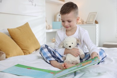 Bedtime. Cute boy with toy sheep reading book on bed indoors