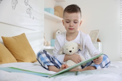 Bedtime. Cute boy with toy sheep reading book on bed indoors