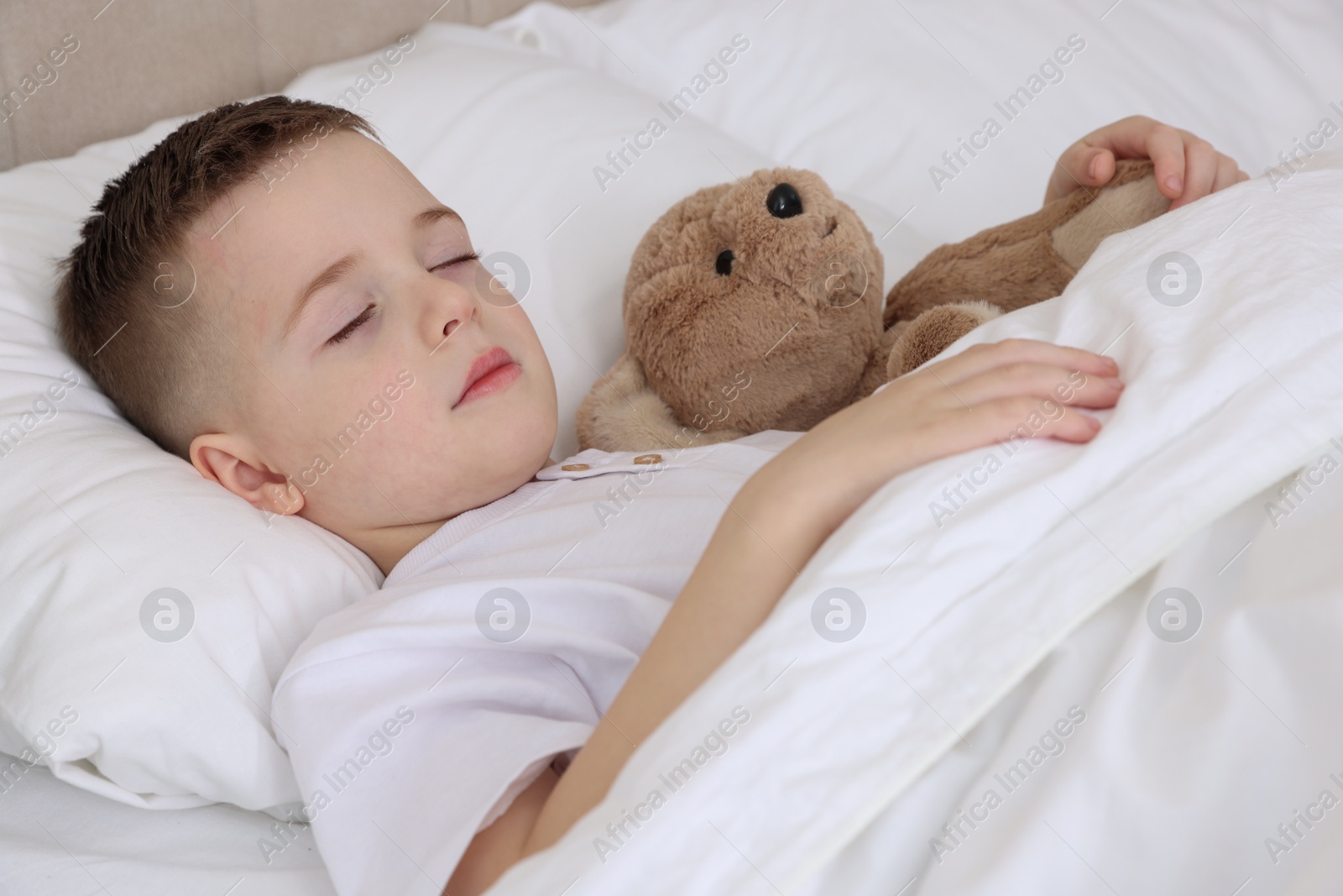 Photo of Bedtime. Cute boy sleeping with his teddy bear in bed