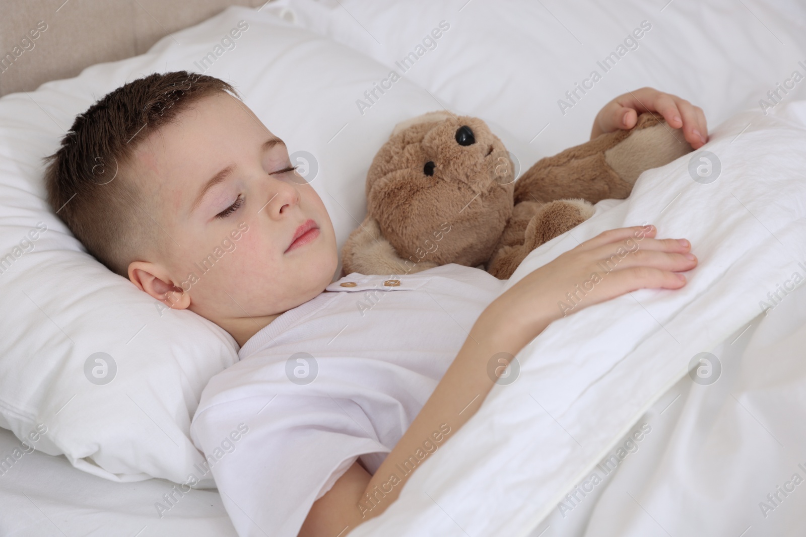 Photo of Bedtime. Cute boy sleeping with his teddy bear in bed