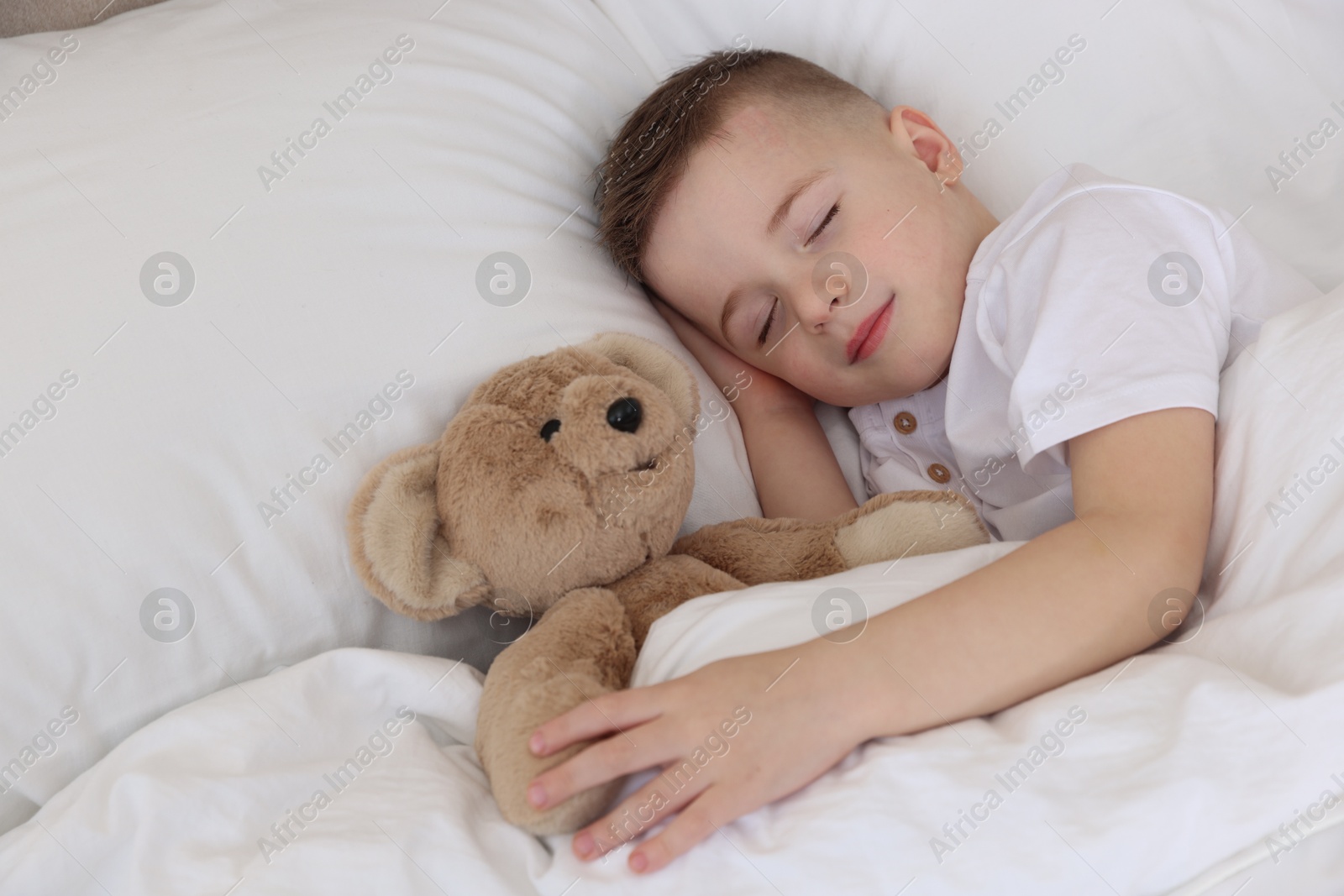 Photo of Bedtime. Cute boy sleeping with his teddy bear in bed