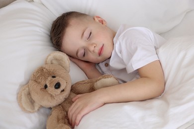 Photo of Bedtime. Cute boy sleeping with his teddy bear in bed