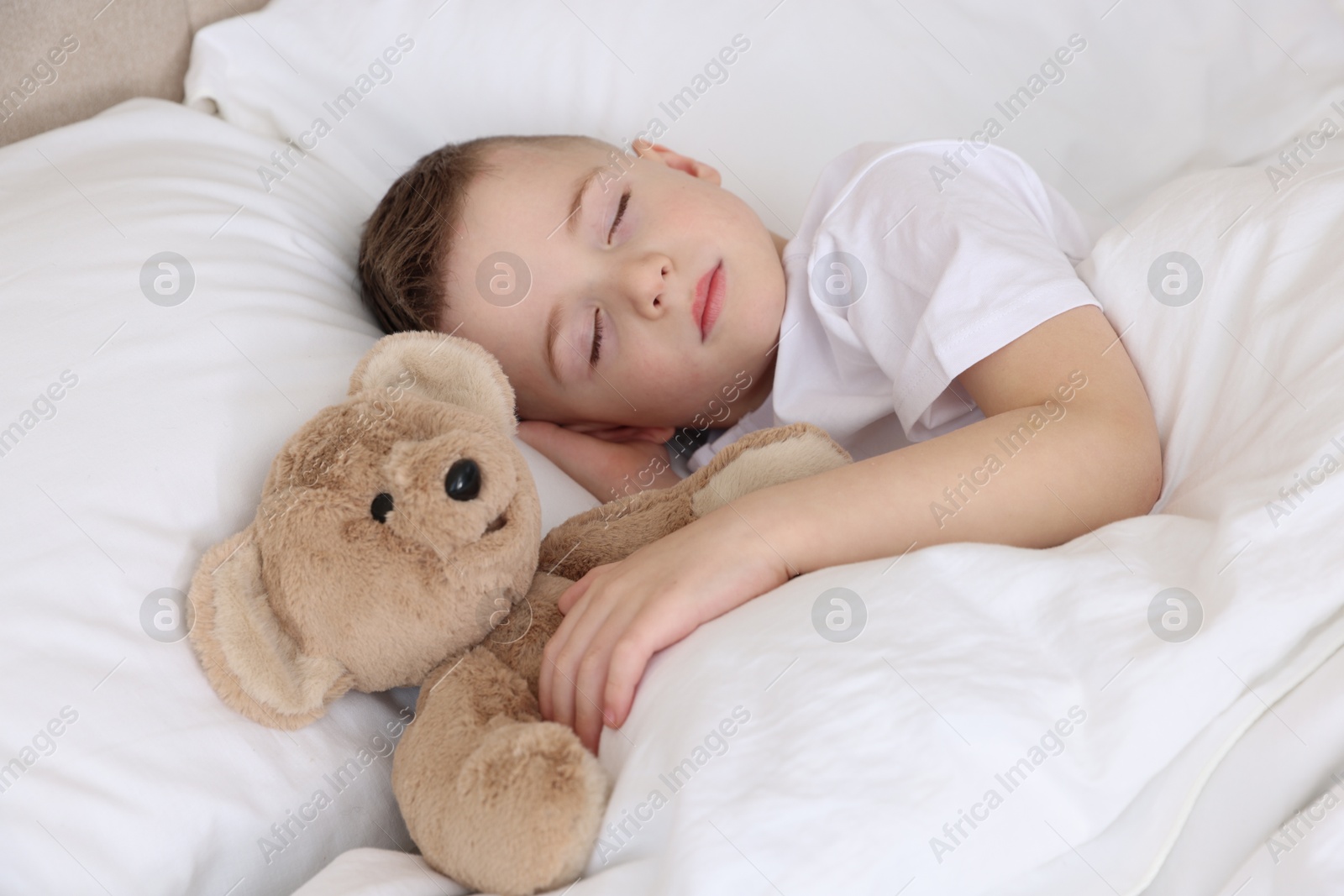 Photo of Bedtime. Cute boy sleeping with his teddy bear in bed