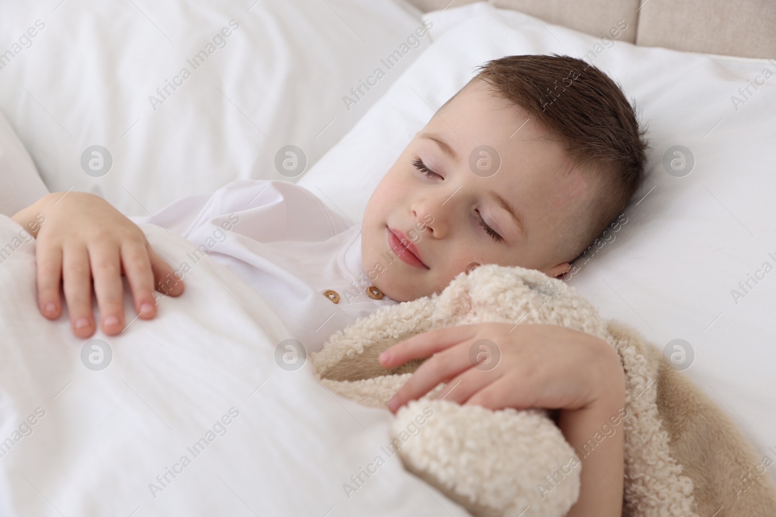 Photo of Bedtime. Cute boy sleeping with toy sheep in bed