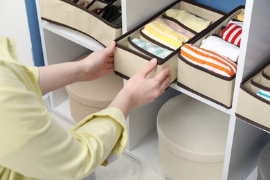 Photo of Woman putting organizer with folded clothes onto shelf at home, closeup