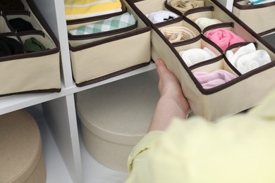 Photo of Woman putting organizer with different socks onto shelf at home, closeup