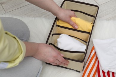 Photo of Woman putting folded clothes into organizer on floor at home, above view