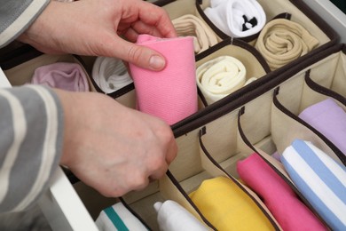 Photo of Woman putting rolled sock into organizer in drawer at home, closeup