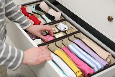 Photo of Woman putting rolled sock into organizer in drawer at home, closeup