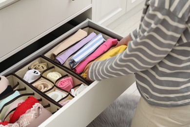 Photo of Woman putting folding clothes into organizer in drawer at home, closeup