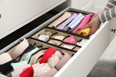 Photo of Woman putting folding clothes into organizer in drawer at home, closeup