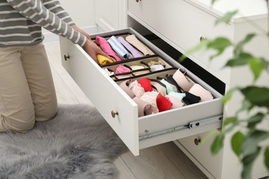 Photo of Woman putting folding clothes into organizer in drawer at home, closeup