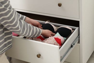 Photo of Woman putting bra into organizer in drawer at home, closeup