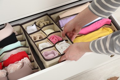 Photo of Woman putting organizer with different socks into drawer at home, closeup