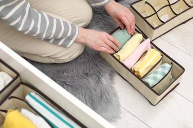 Photo of Woman putting folded clothes into organizer on floor at home, above view