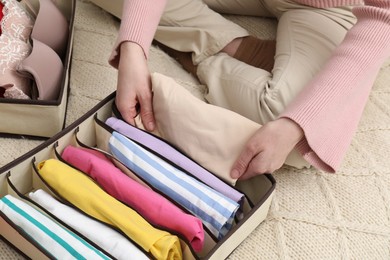 Woman putting folded clothes into organizer on bed at home, above view