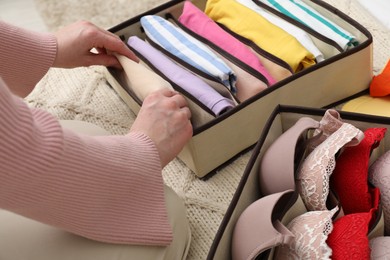 Woman putting folded clothes into organizer on bed at home, closeup