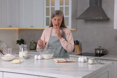 Senior woman with recipe book cooking in kitchen