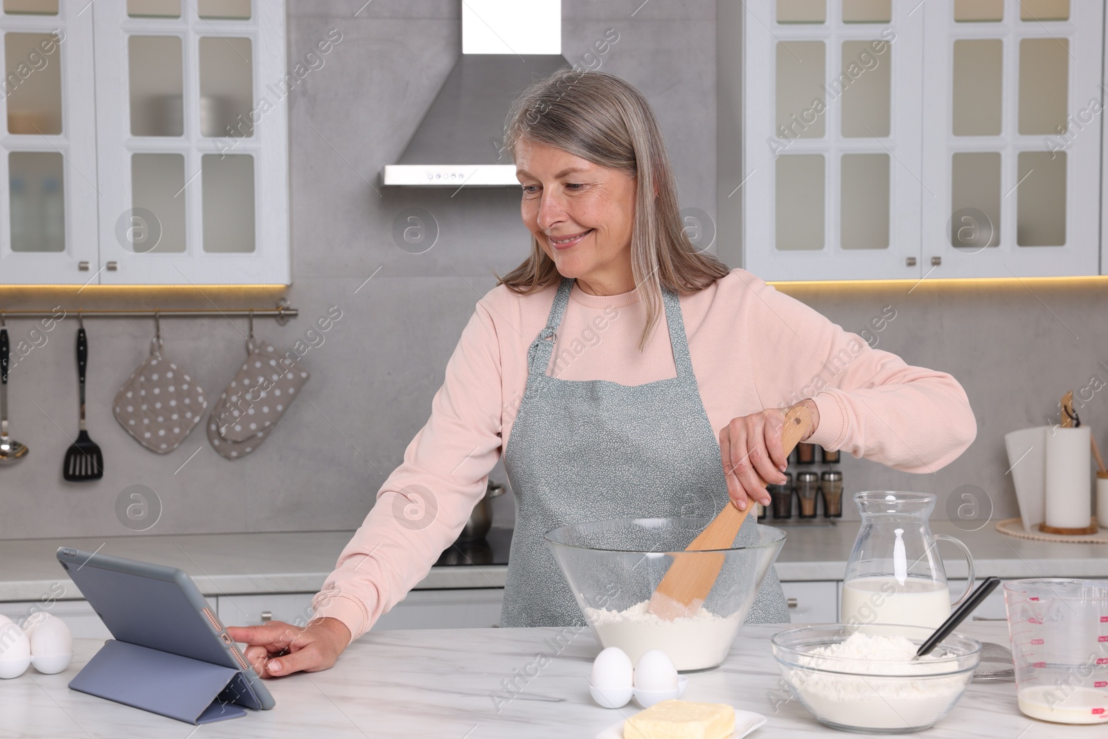 Photo of Senior woman reading recipe on tablet while cooking in kitchen. Online culinary book