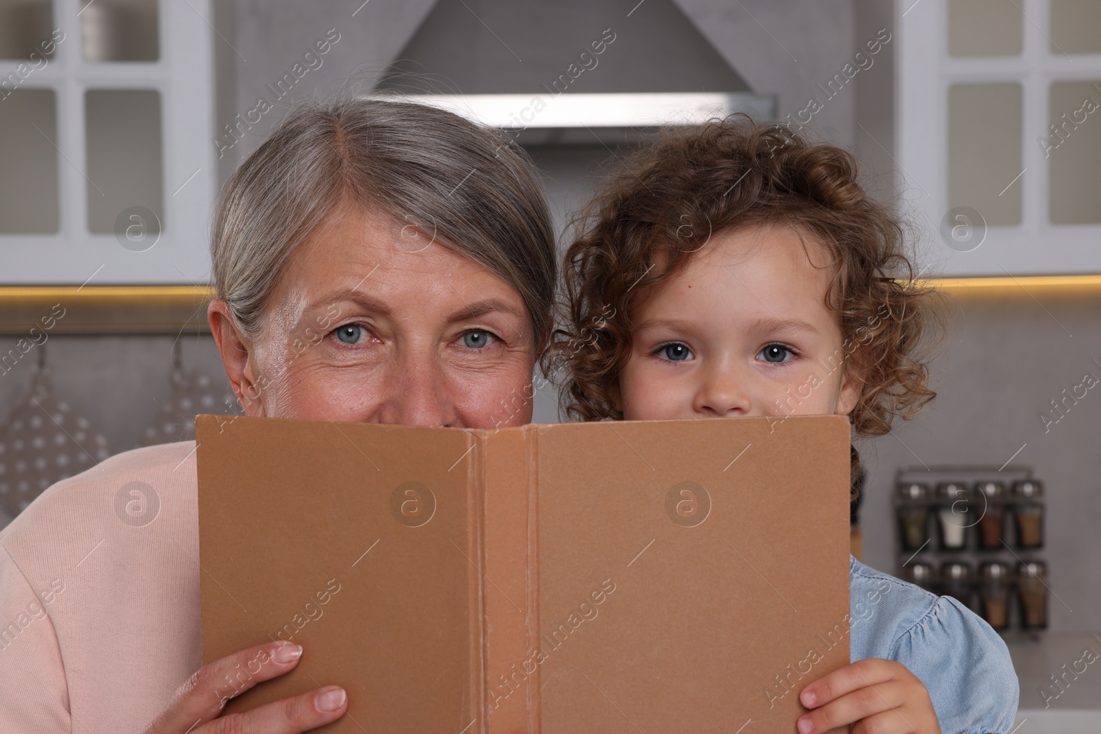 Photo of Cute little girl and her granny with recipe book in kitchen