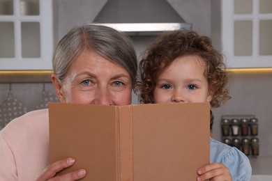 Cute little girl and her granny with recipe book in kitchen