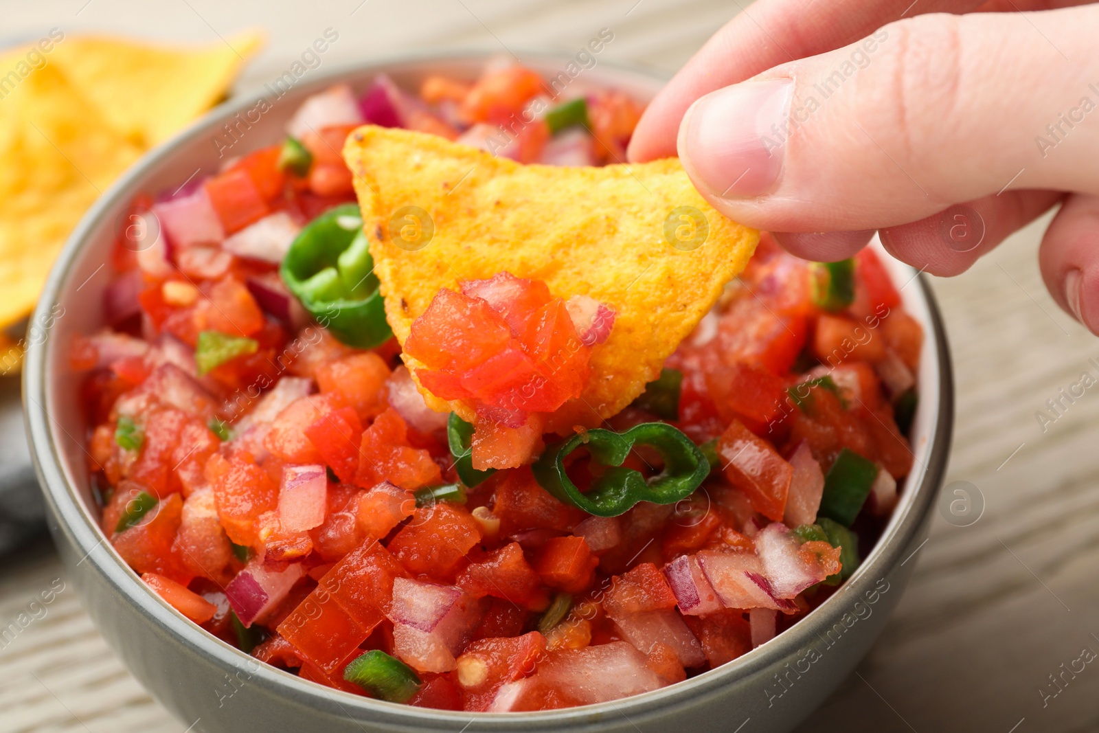 Photo of Woman dipping nacho chip into delicious salsa sauce at table, closeup