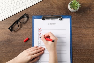 Woman filling Checklist at wooden table, top view