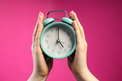 Photo of Woman with turquoise alarm clock on bright pink background, closeup