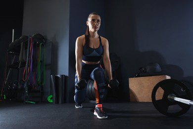 Sportswoman exercising with dumbbells during crossfit workout in gym