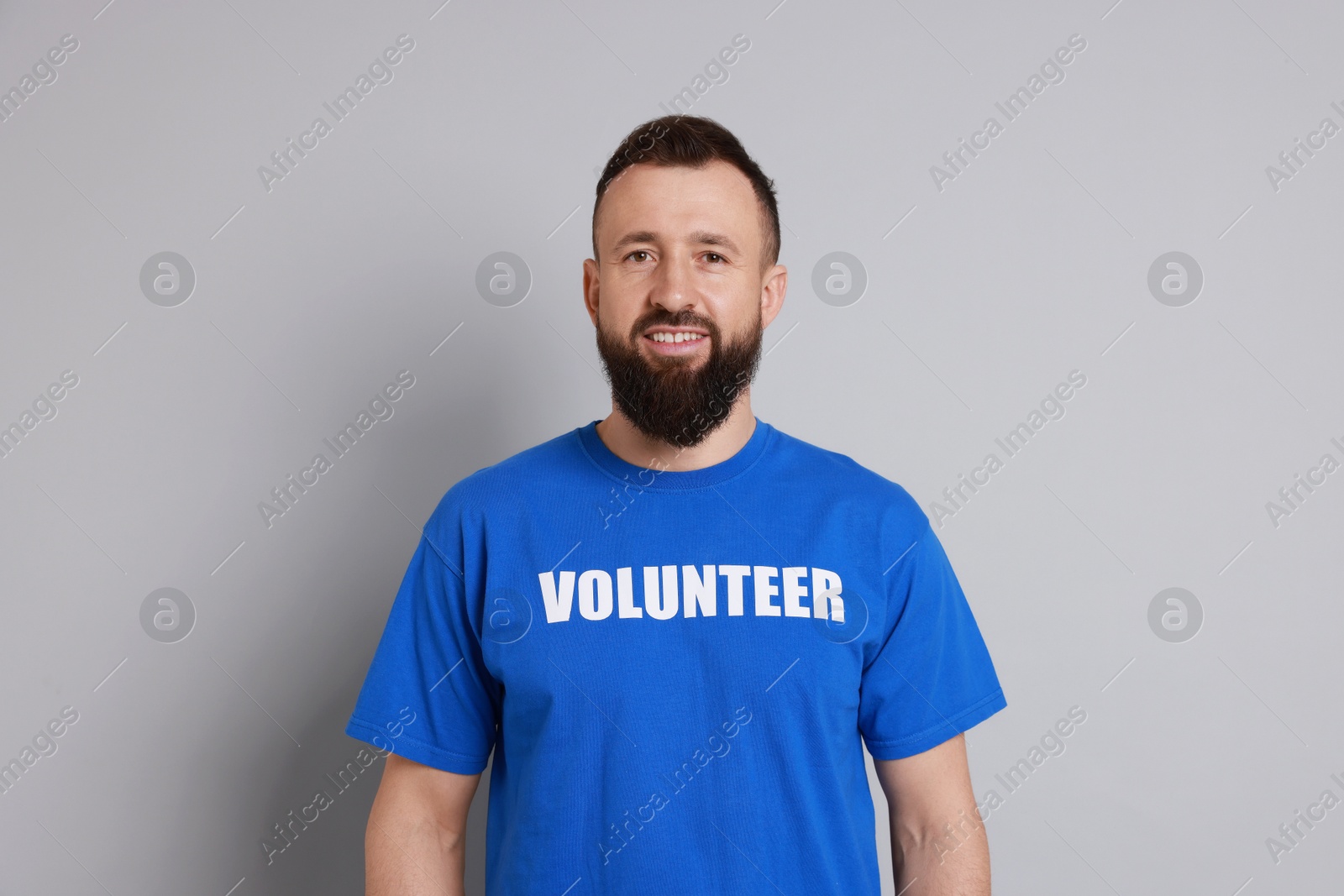 Photo of Positive man wearing t-shirt with word Volunteer on light grey background