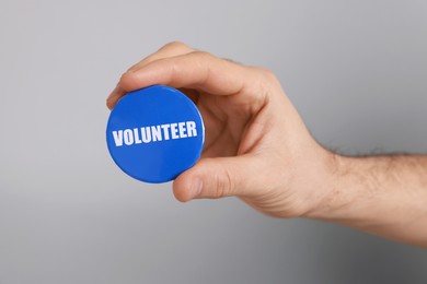 Photo of Man holding button badge with word Volunteer on light grey background, closeup