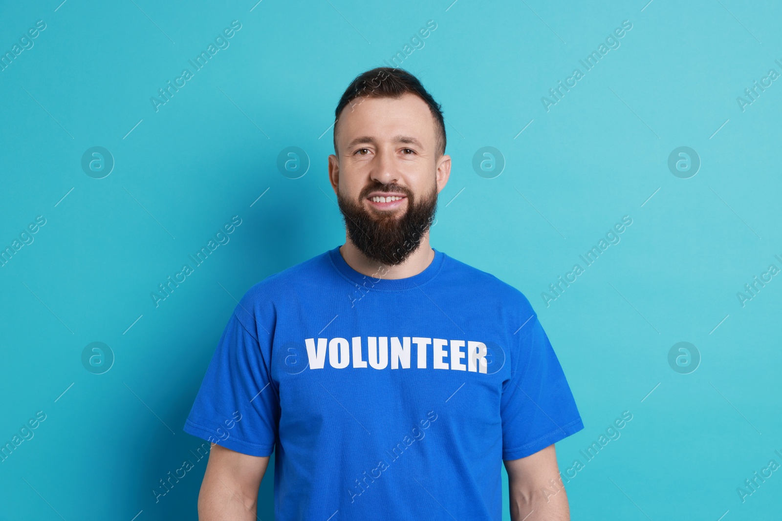 Photo of Positive man wearing t-shirt with word Volunteer on light blue background