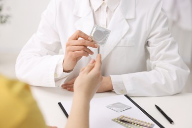 Photo of Contraception. Gynecologist recommending condom to woman in clinic, closeup