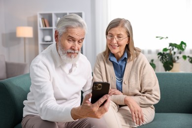 Photo of Happy elderly couple with smartphone on sofa at home