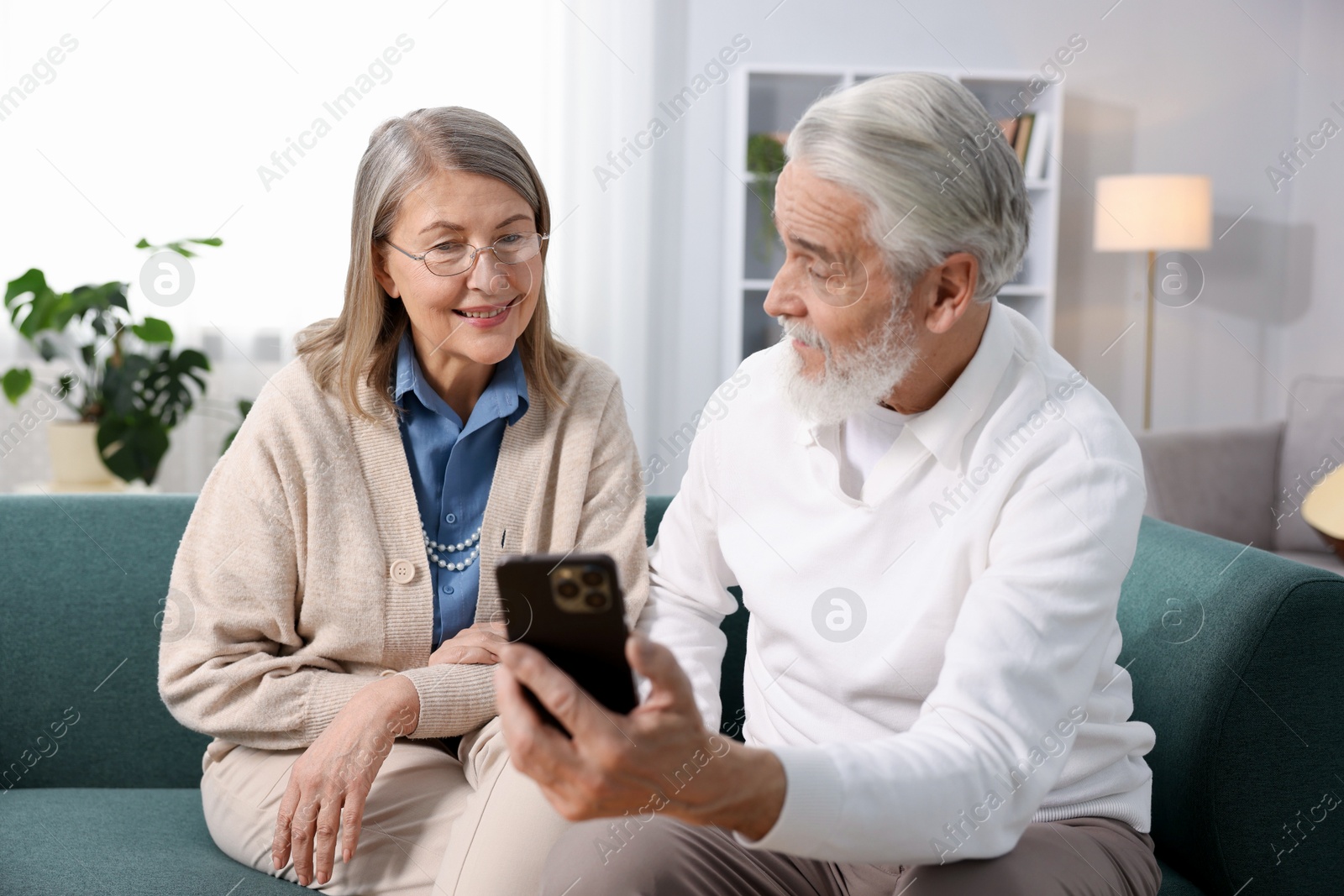 Photo of Happy elderly couple with smartphone on sofa at home